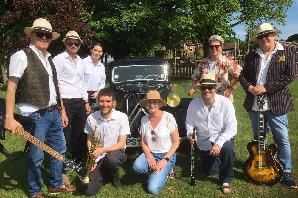 An eight piece band in the sunshine smiling