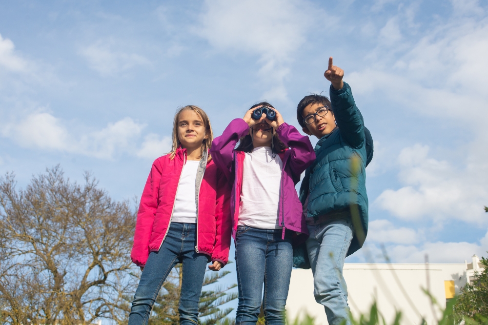 A group of three children using binoculars in an outdoor park setting